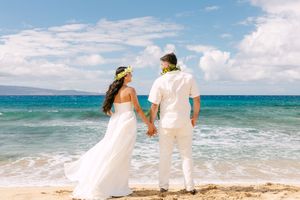 Newlyweds hold hands while gazing at the turquoise ocean during their Hawaiian beach wedding in Maui.