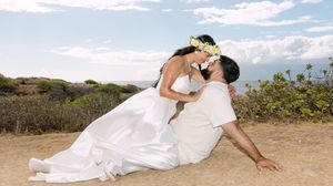 Bride and groom share a passionate kiss while sitting on a sun-drenched hillside in Maui Hawaii.