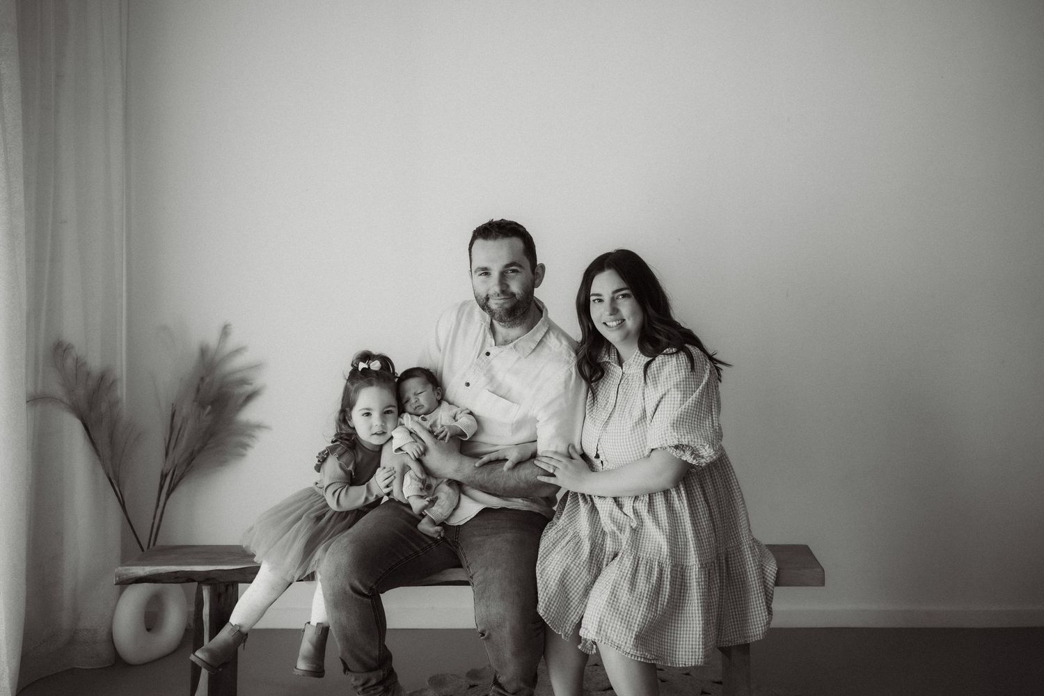 Black and white family portrait with parents and two young children sitting together in a bright minimalist studio in Healesville, Victoria