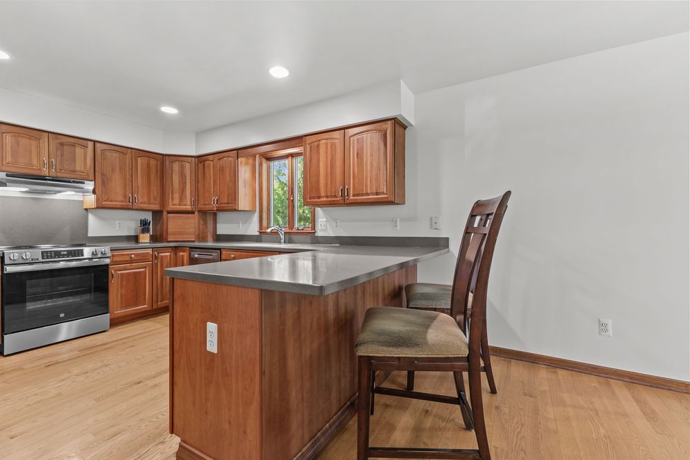 Kitchen with wood cabinets, dark countertops, island with seating, stainless appliances, and hardwood floors.