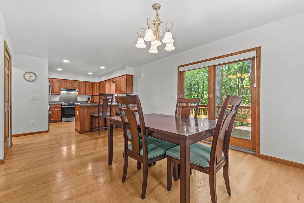 Bright dining area with chandelier, hardwood floors, wood chairs, and sliding door to outdoor deck.