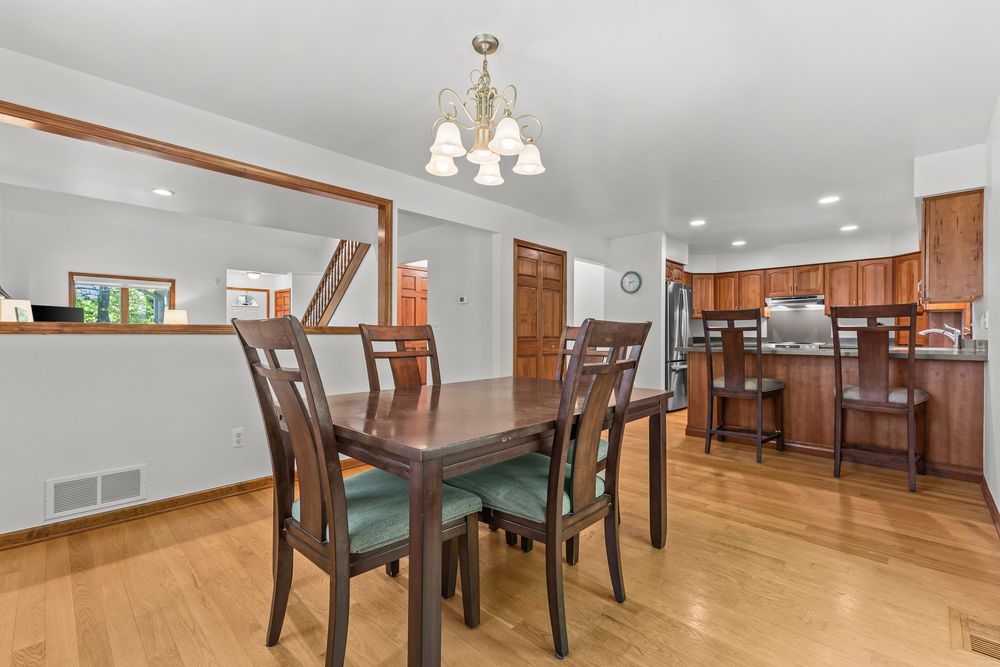 Open dining room with wood table, chandelier, hardwood floors, and view into kitchen with wood cabinets.