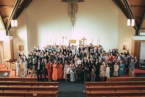 Large group photo of wedding guests gathered inside a traditional church with wooden pews and altar.