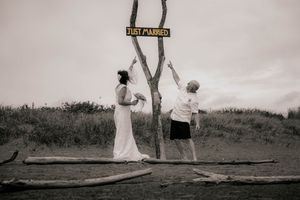 Newlywed couple posing by a Just Married sign on a tree at a beach wedding in black and white photo.