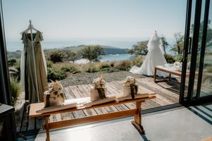 Elegant outdoor wedding venue with ocean views, featuring a wooden bench, floral arrangements, and bridal gown on a deck.