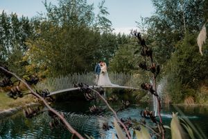 Bride and groom embracing on a rustic bridge over a pond surrounded by lush greenery on their wedding day.