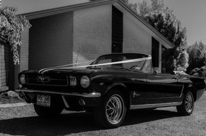 Classic black Ford Mustang convertible parked outside a building in a vintage black and white photograph.