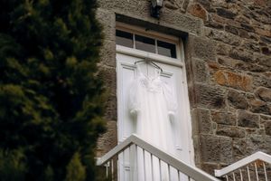 White wedding dress hanging on a decorative white door of a rustic stone building with steps.