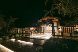 Elegant resort building illuminated at night with warm lights, surrounded by tropical plants and a sleek stone pathway.