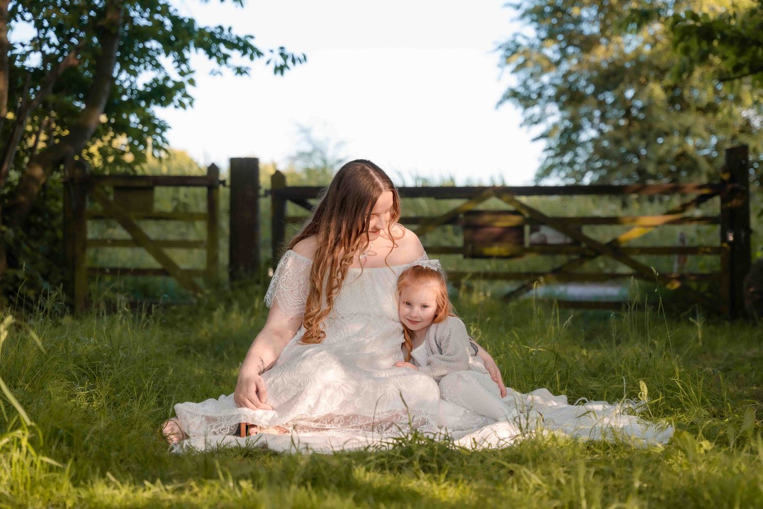 Family of four sitting on blanket in forest, parents smiling at baby and toddler in warm autumn setting.