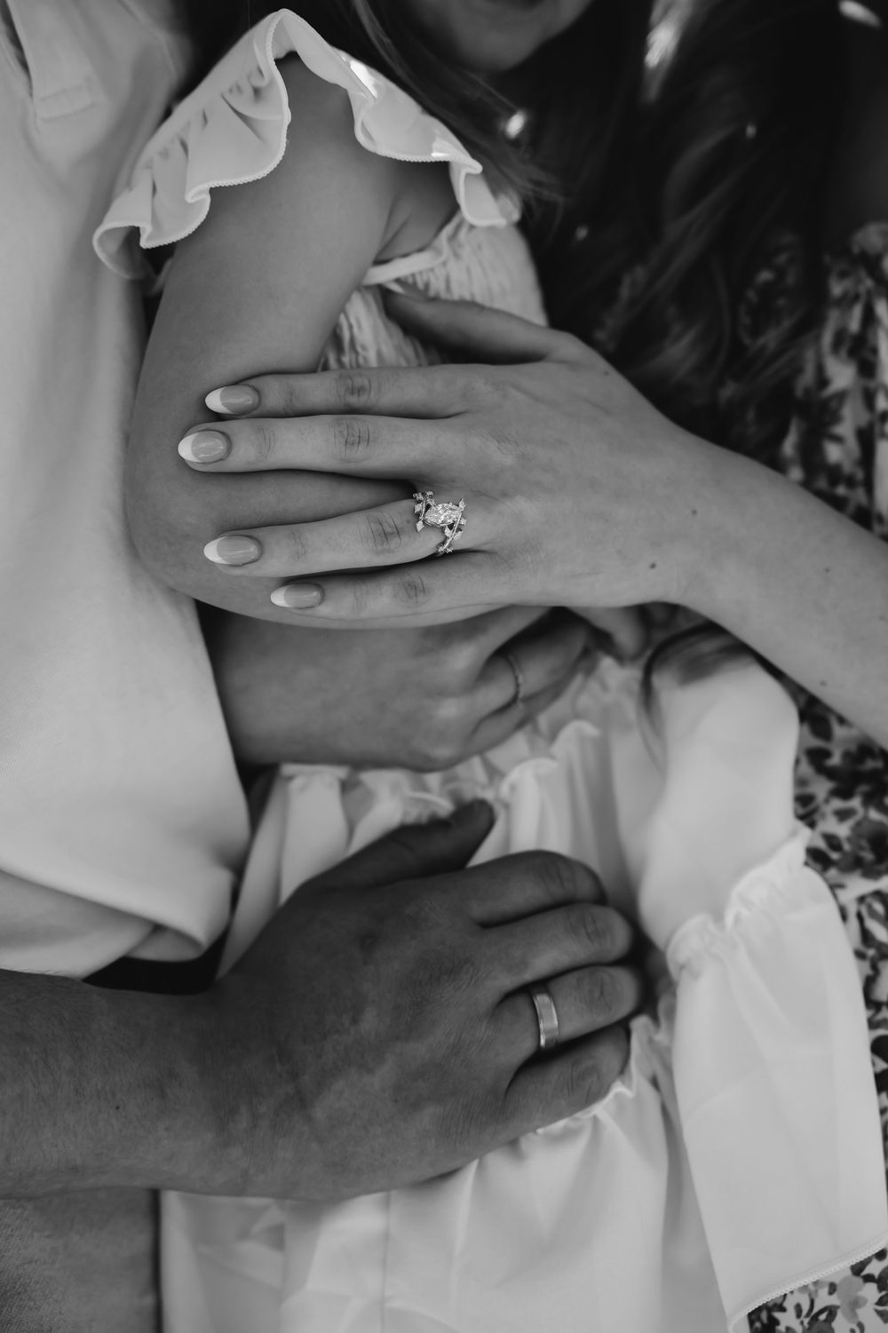 Black and white photo of a couple embracing, showcasing an engagement ring and wedding band on their hands.