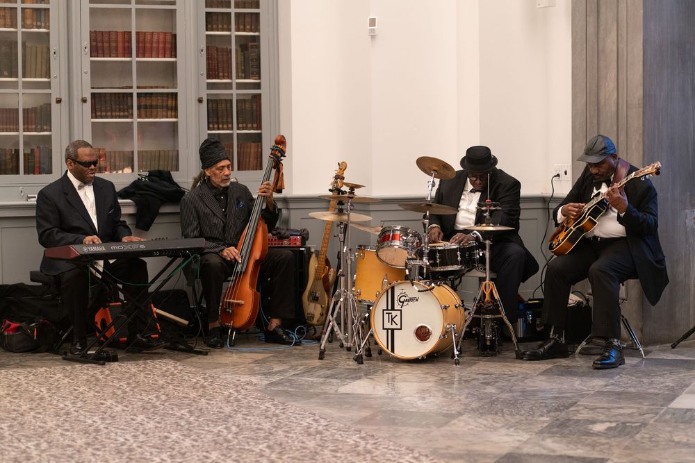 Jazz quartet performing with keyboard, bass, drums, and guitar in an elegant hall.