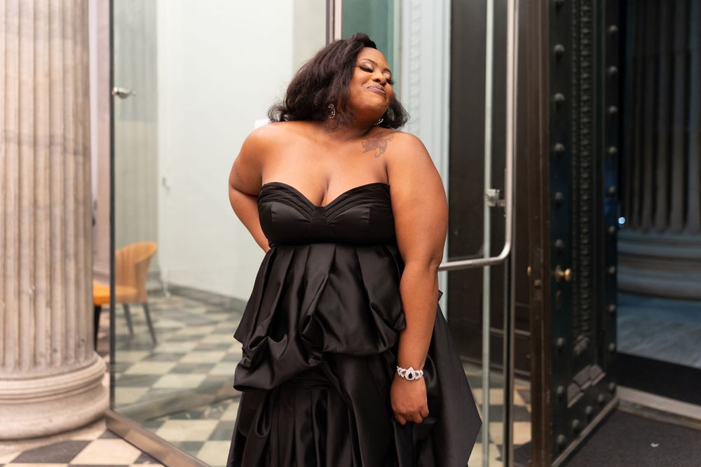 Woman in elegant black strapless ruffled gown posing confidently near a column at a formal event.