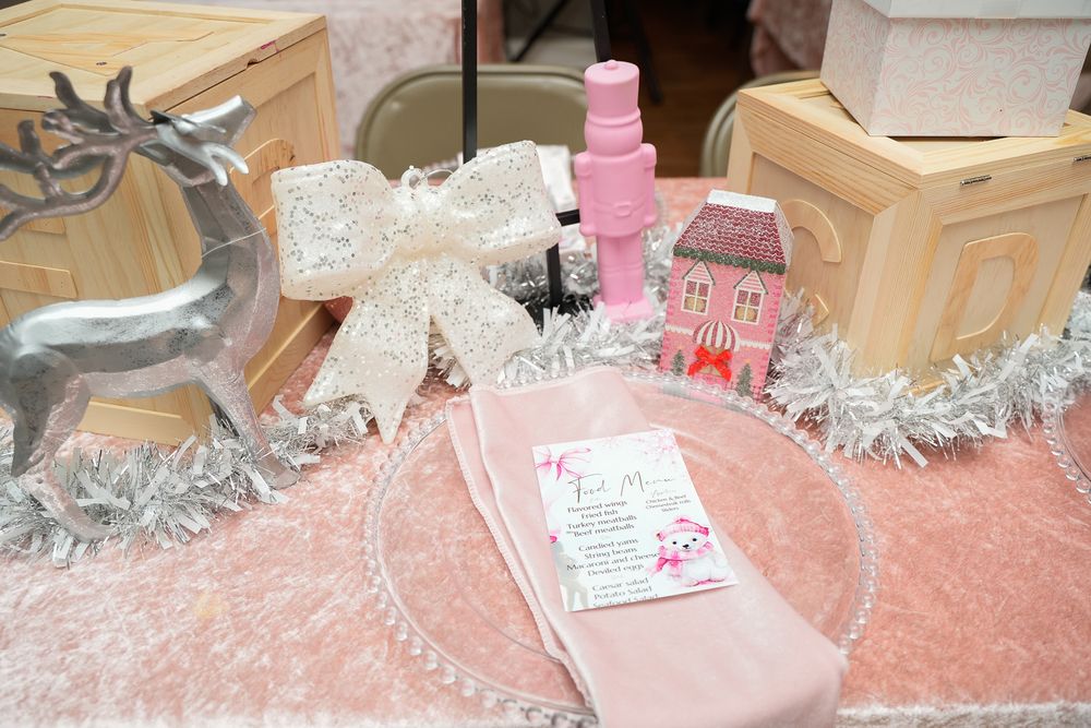 Pink Christmas baby shower table with silver reindeer, glitter bow, pink house figurine, and elegant place setting.