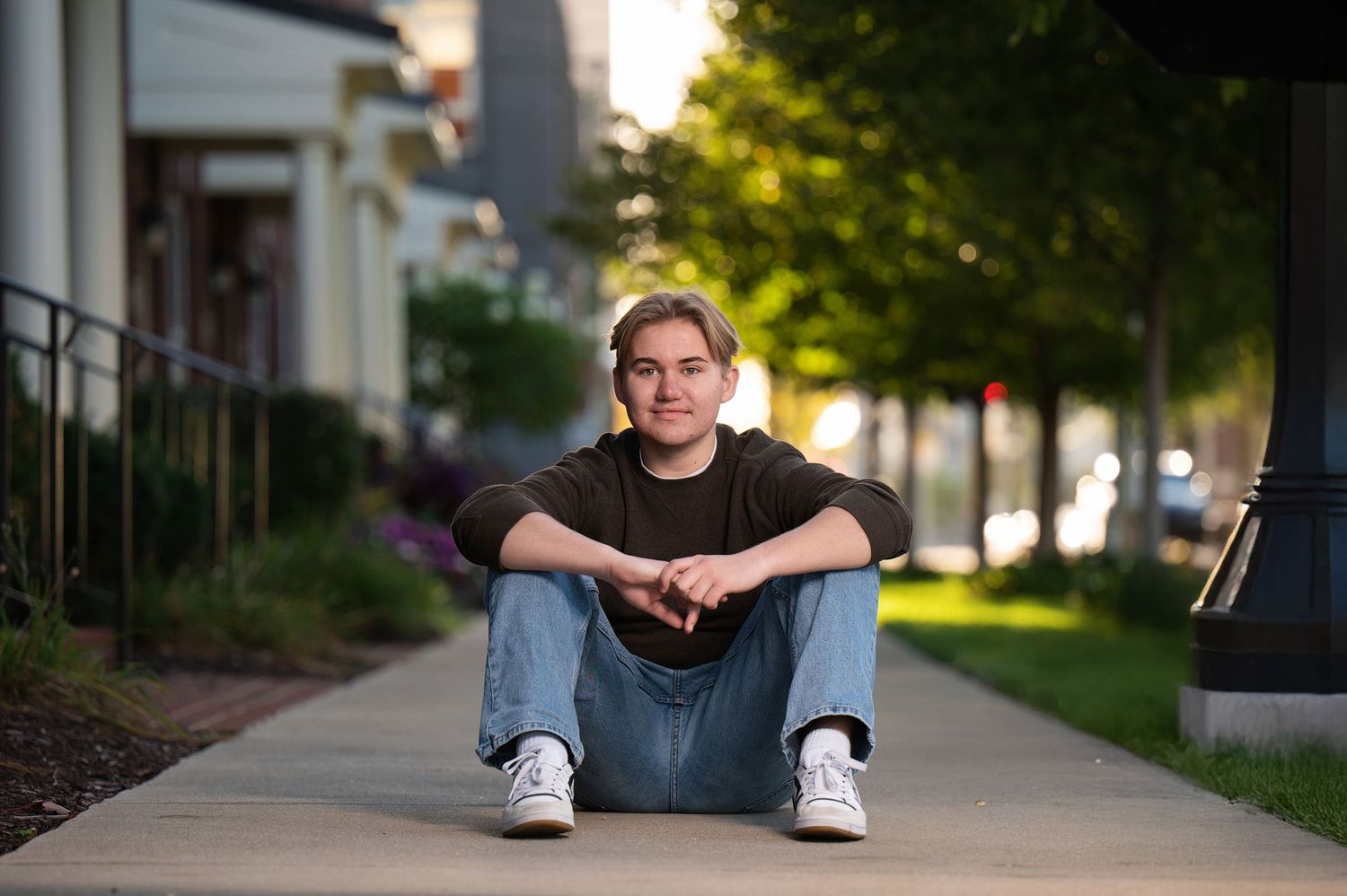 A young person sitting on steps, laughing joyfully, wearing a dark sweater and jeans, in a black and white photo.