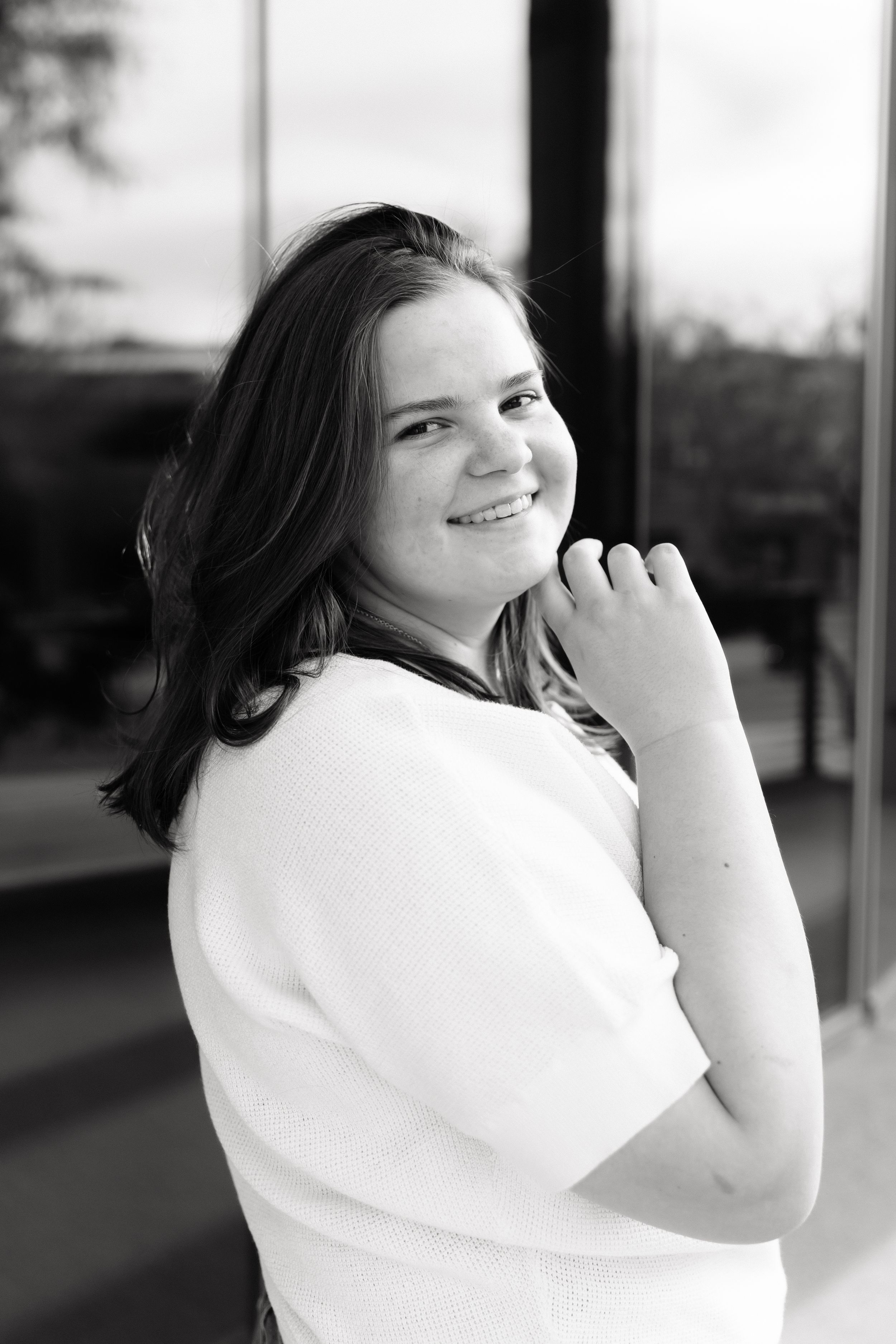 Young woman in white top smiling over shoulder in black and white portrait photo outdoors.