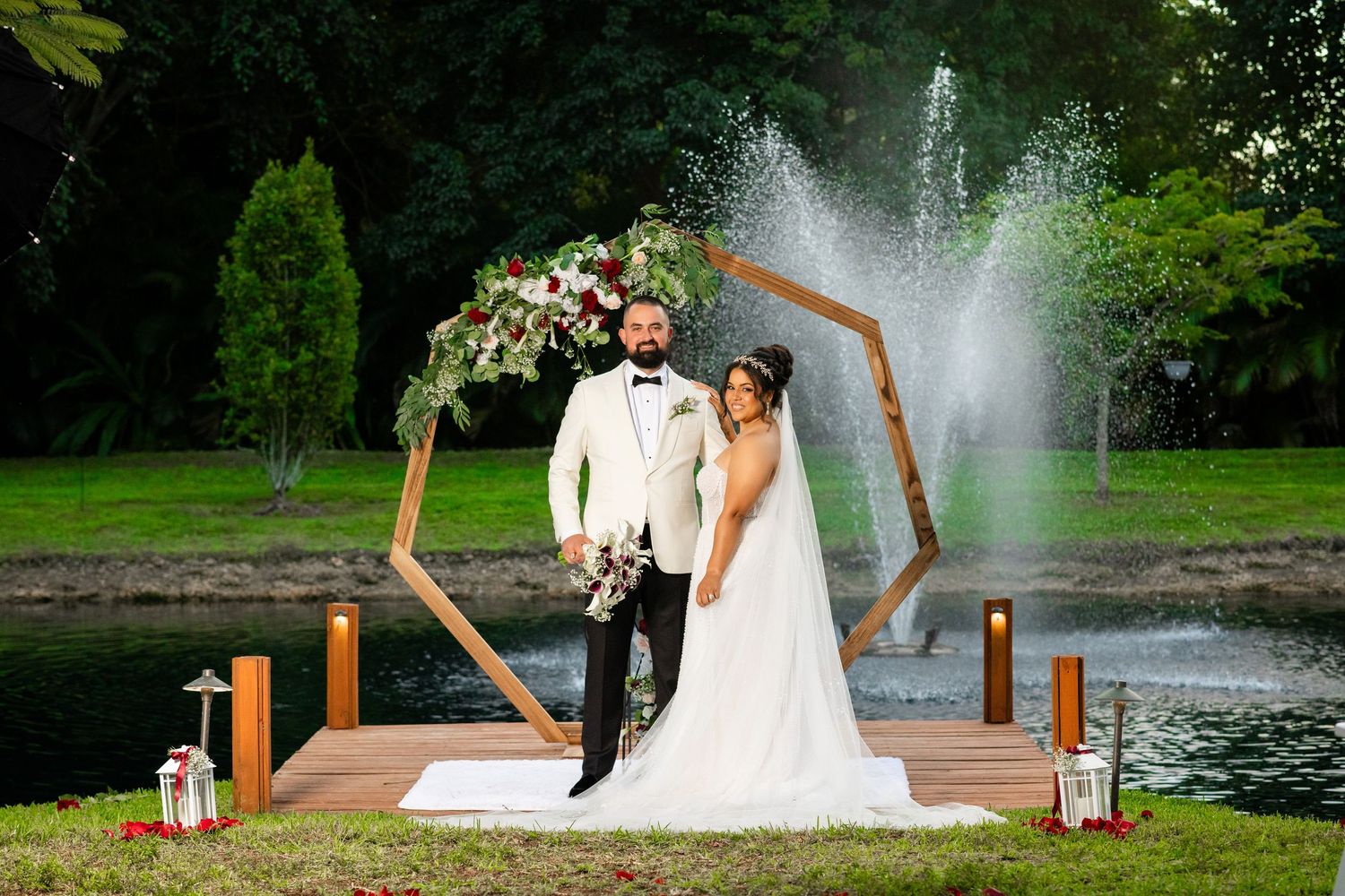 Stylish man in white tuxedo jacket and bow tie posing confidently against a dark blue background.