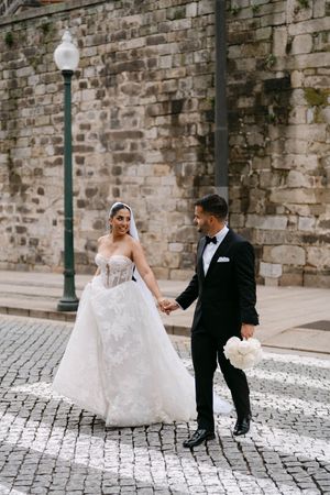 A romantic wedding couple poses on cobblestone streets against a historic stone wall backdrop.