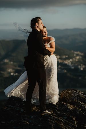 Romantic sunset wedding photos of couple embracing on mountain peak with dramatic landscape views.