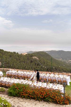Outdoor wedding reception setup with white tables and mountain views in the background.