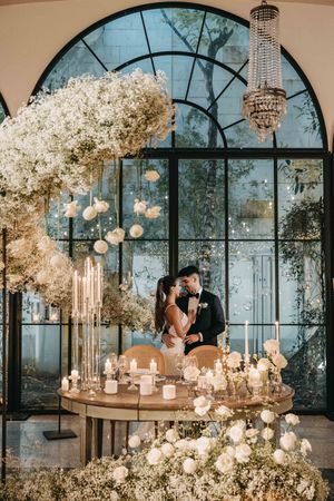 Elegant wedding reception setup with crystal chandelier, baby's breath floral arrangements and romantic candlelight in glass atrium.