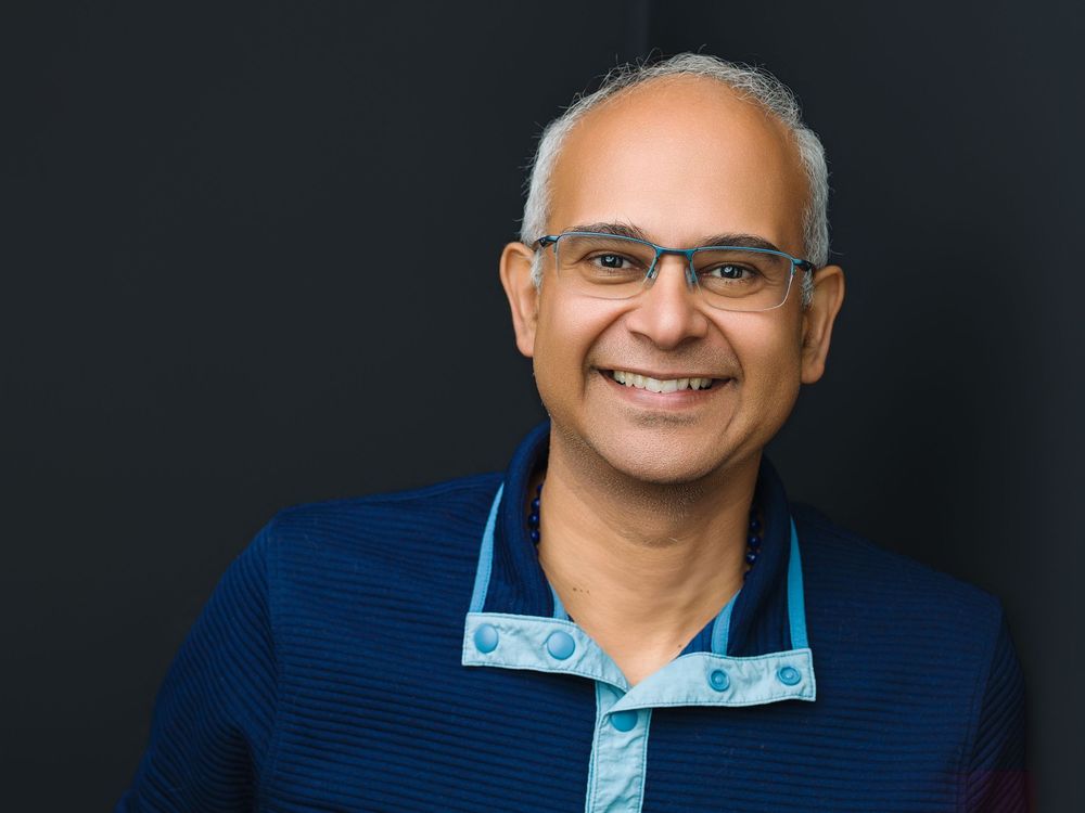 Smiling middle-aged man with glasses wearing a blue polo shirt poses for a professional headshot photo.