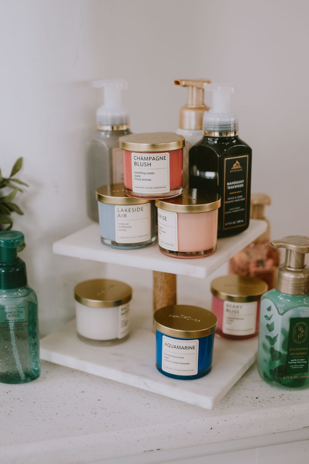 A tiered white marble stand displaying scented candles including Champagne Blush and Aquamarine, with Bath & Body Works lotions nearby.