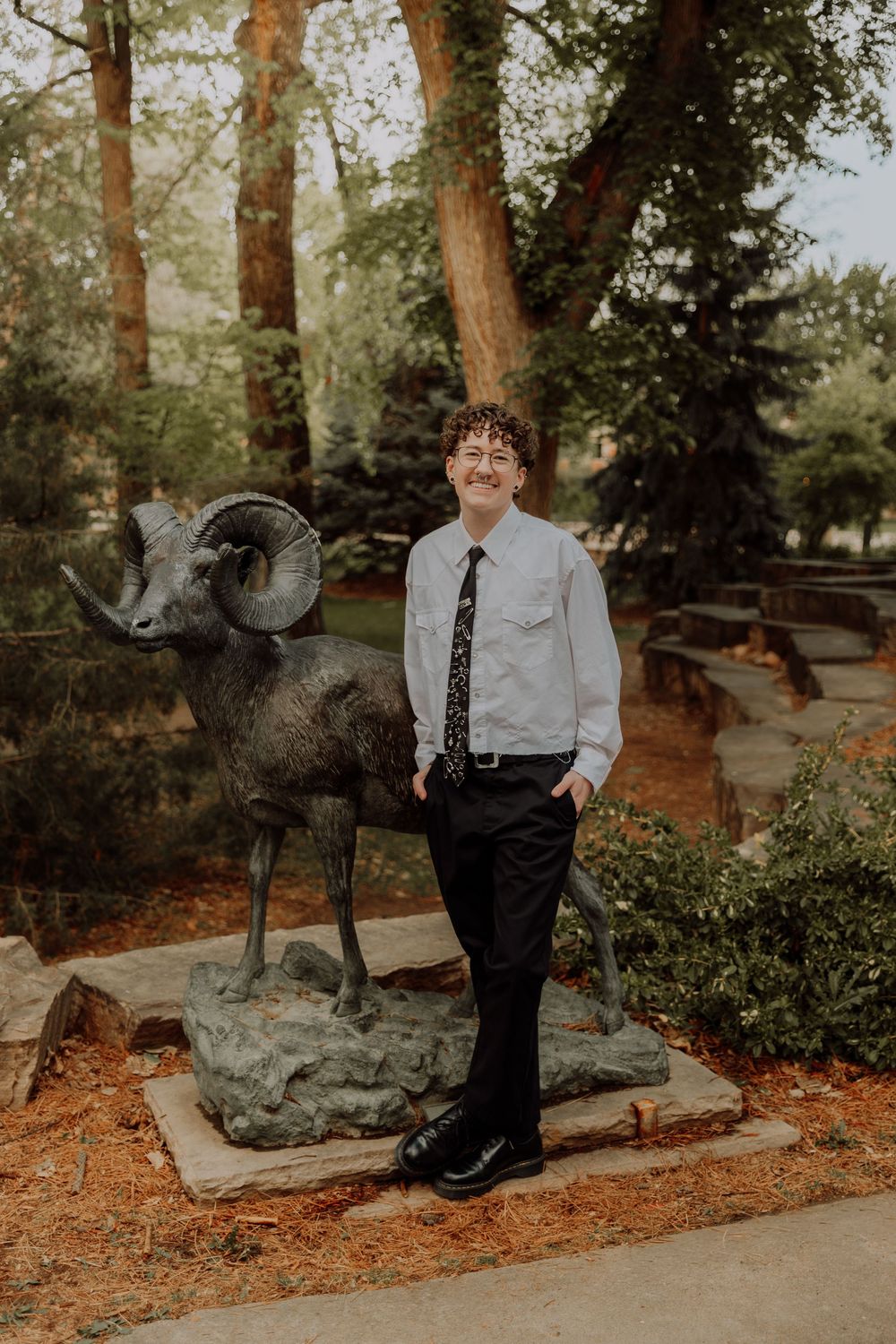 Boy stands and poses by statue for graduation photos at CSU (Colorado State University) graduation photos in Fort Collins, Colorado