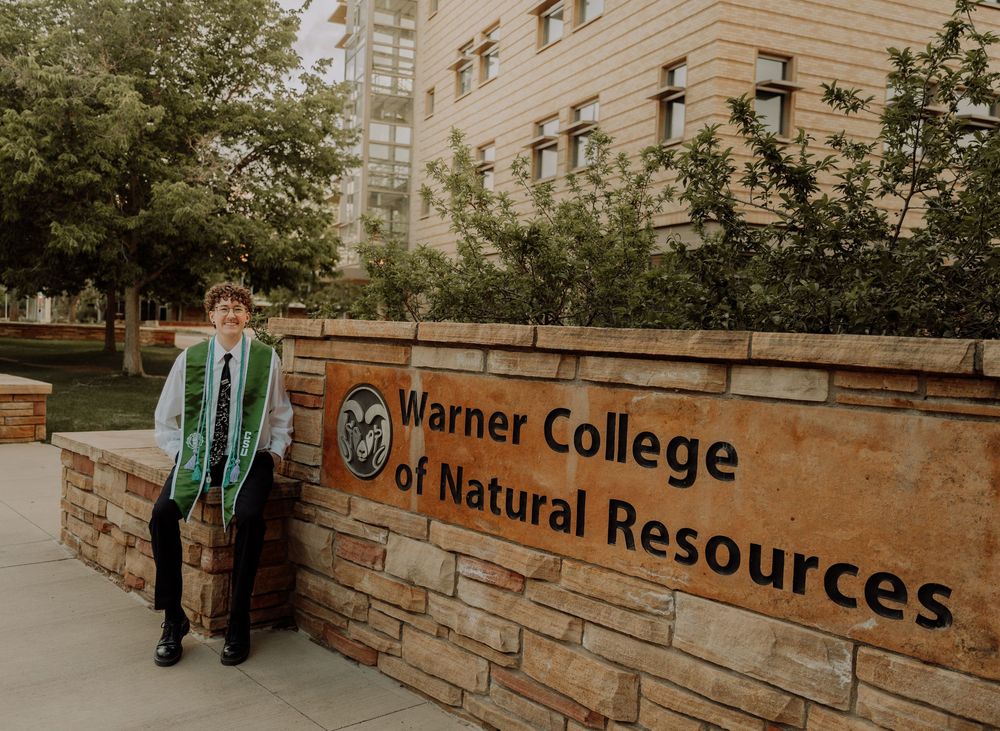 Boy sits and poses by sign for graduation photos at CSU (Colorado State University) graduation photos in Fort Collins, Colorado