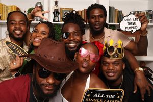 Group of seven friends pose with fun props including a football and speech bubble signs at a party.