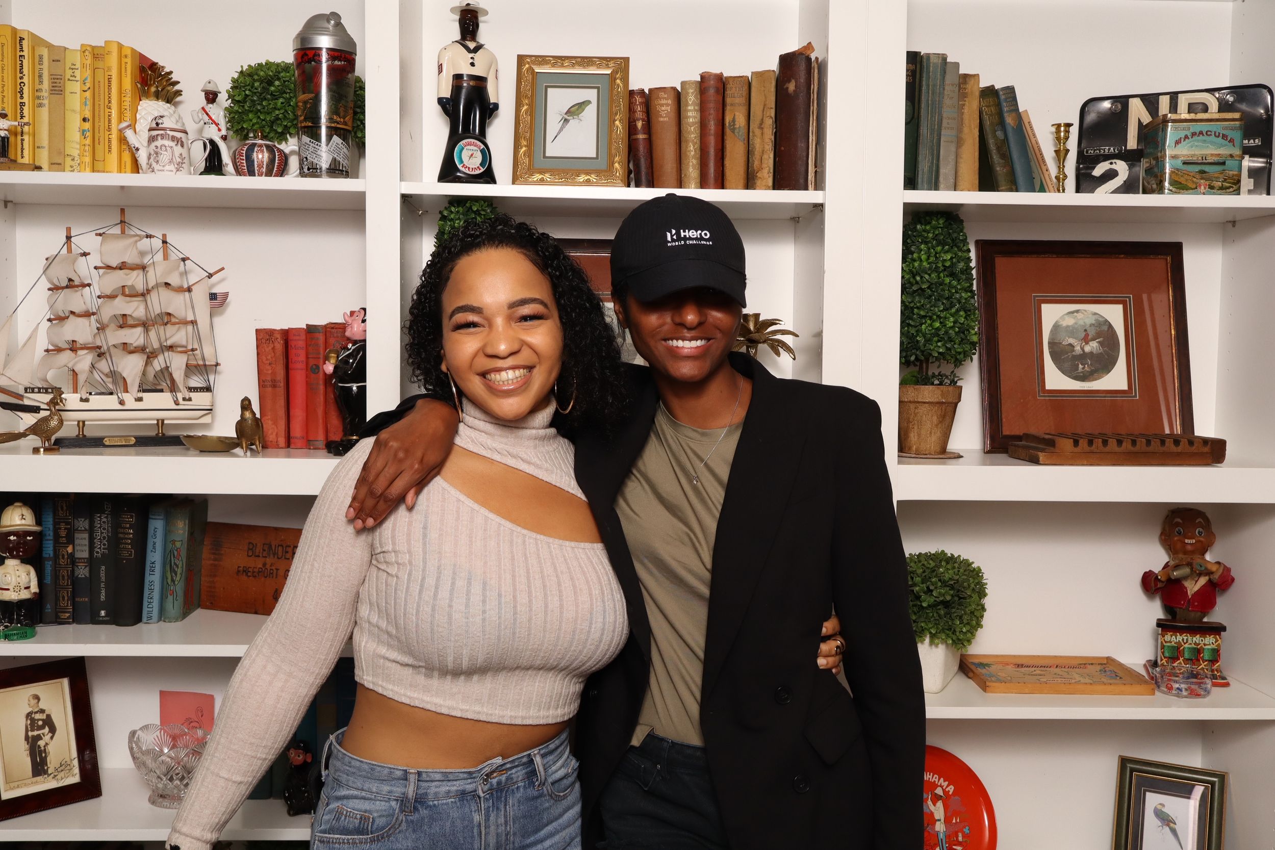 Two friends smiling and posing together in front of a decorative bookshelf filled with books and decor.