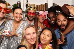 Group of diverse friends posing together at a party wearing fun accessories like novelty glasses and hats.