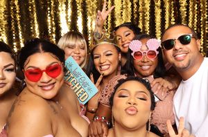 Group of friends posing in a photo booth with fun glasses and props in front of a gold sequin backdrop.