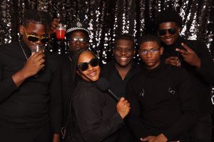 Six friends in black outfits pose and smile in front of a silver sequin backdrop at a festive party event.