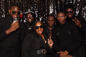 Group of six friends posing together in all-black outfits at a glamorous event with sequin backdrop.