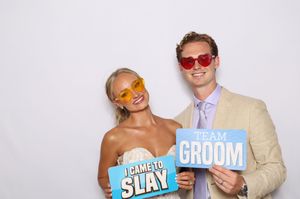 Bride and groom posing in photo booth holding fun signs reading I Came to Slay and Team Groom wearing colorful sunglasses.