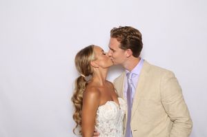 Bride and groom sharing a romantic kiss at their wedding, dressed in lace gown and tan suit.