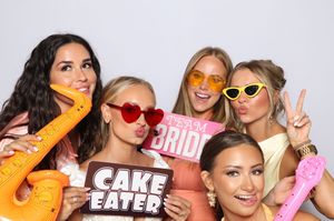 Five women pose playfully at a bachelorette photo booth holding fun signs including Cake Eater and Team Bride.
