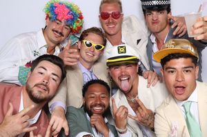Group of men in fun accessories and hats posing together at a photo booth celebration.
