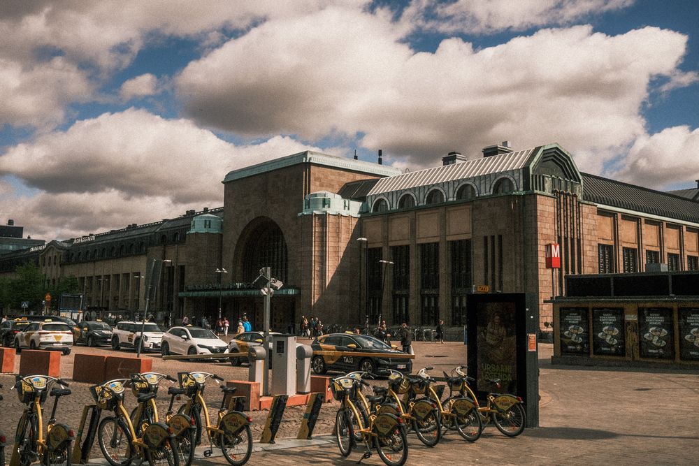 Bicycles parked outside a historic brick building with arched windows under dramatic cloudy skies in Helsinki.