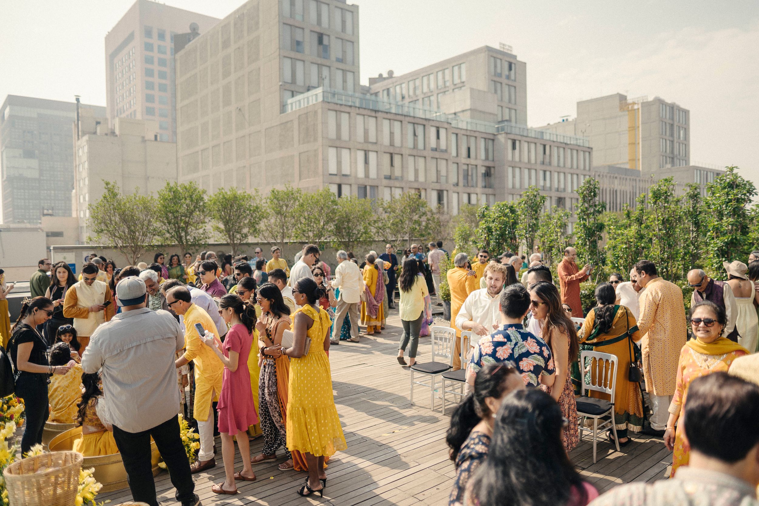 Guests in yellow attire gather on a rooftop terrace for an outdoor celebration with city buildings in the background.