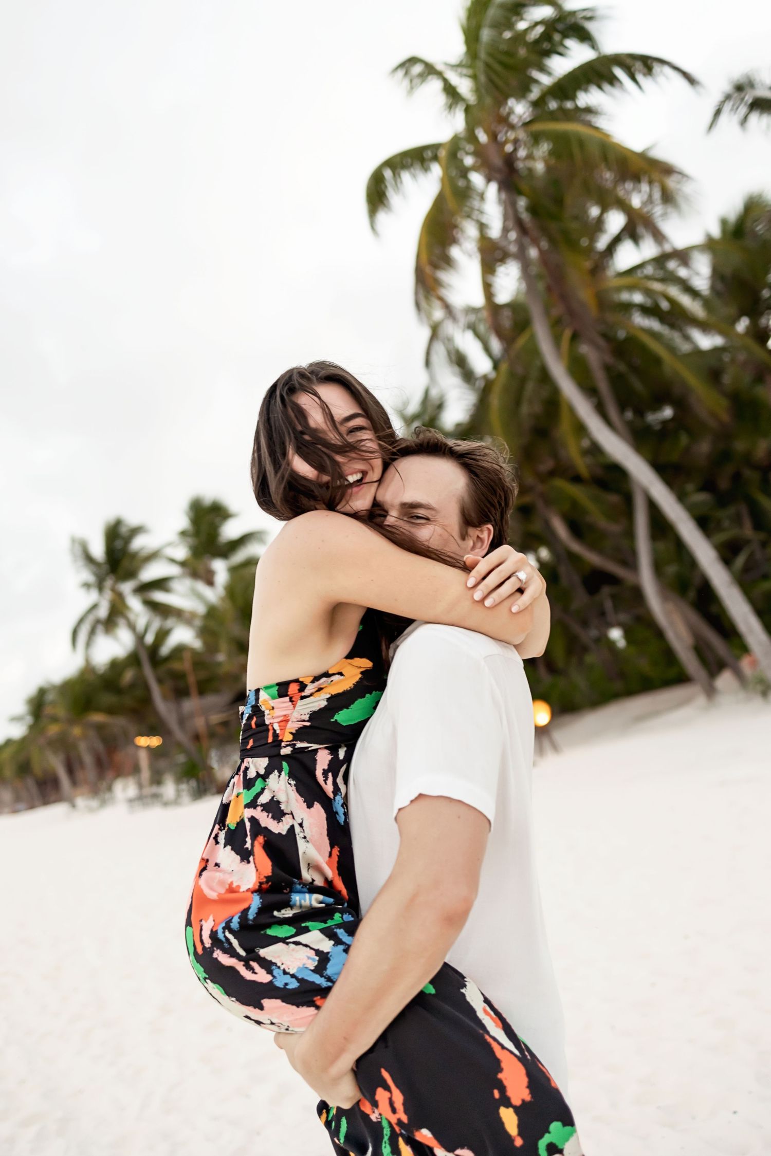 Newly engaged couple embracing after a romantic beach proposal at The Beach Tulum Hotel in Tulum, Mexico surrounded by palm trees.