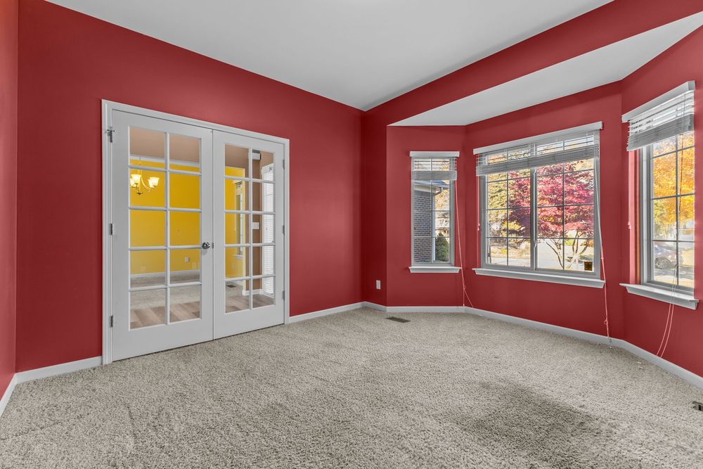 Red-walled carpeted room with French doors, large windows, and natural light creating a warm, inviting living space.