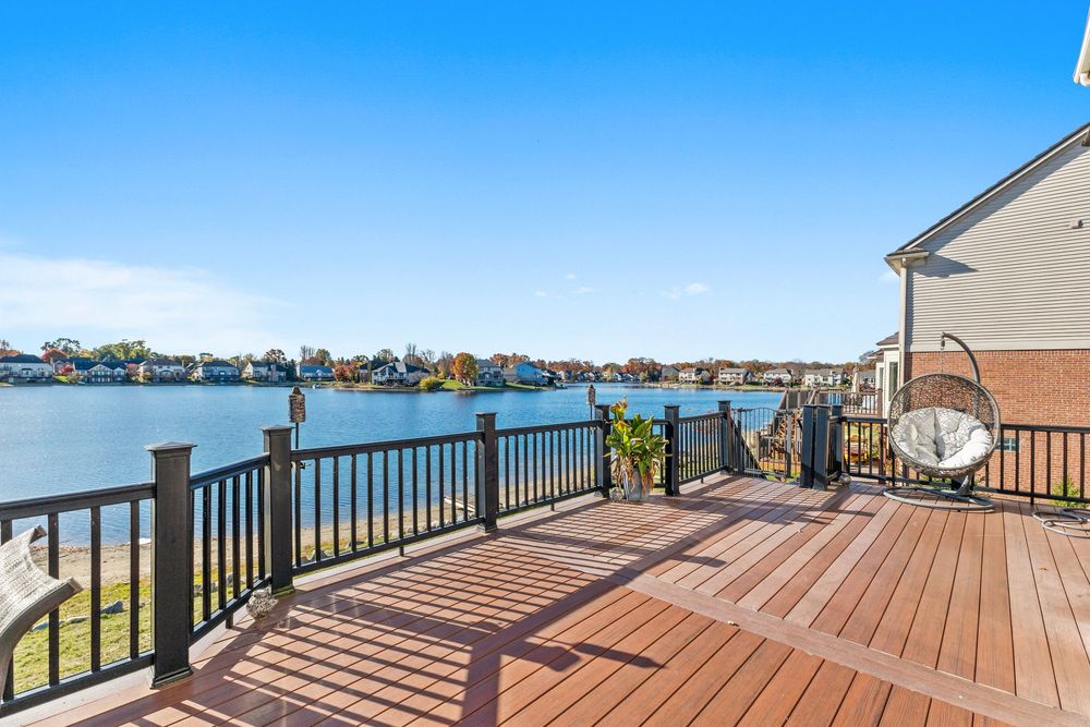 Spacious wooden deck with dark railings overlooking a serene waterfront view under a clear blue sky.