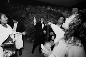 Black and white wedding reception photo of guests dancing and celebrating joyfully indoors.