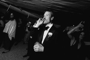 Man in tuxedo smoking cigar at formal wedding reception party, black and white photography.