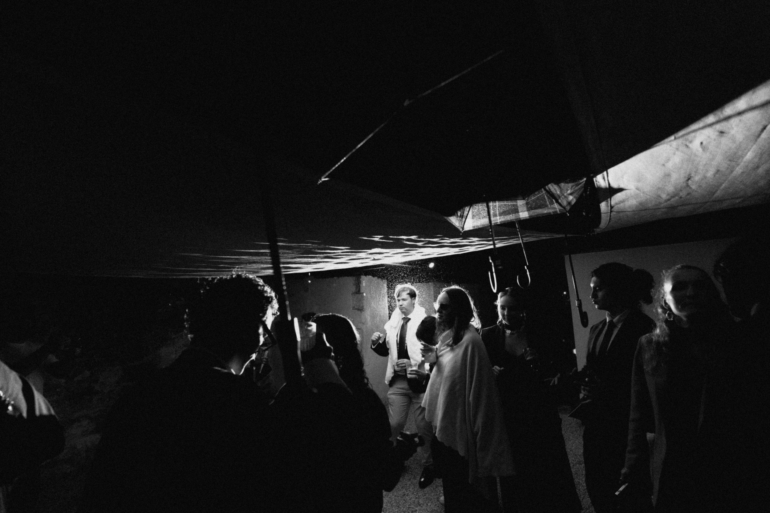 Black and white wedding photo of guests gathered under a tent at night, illuminated by soft lighting.