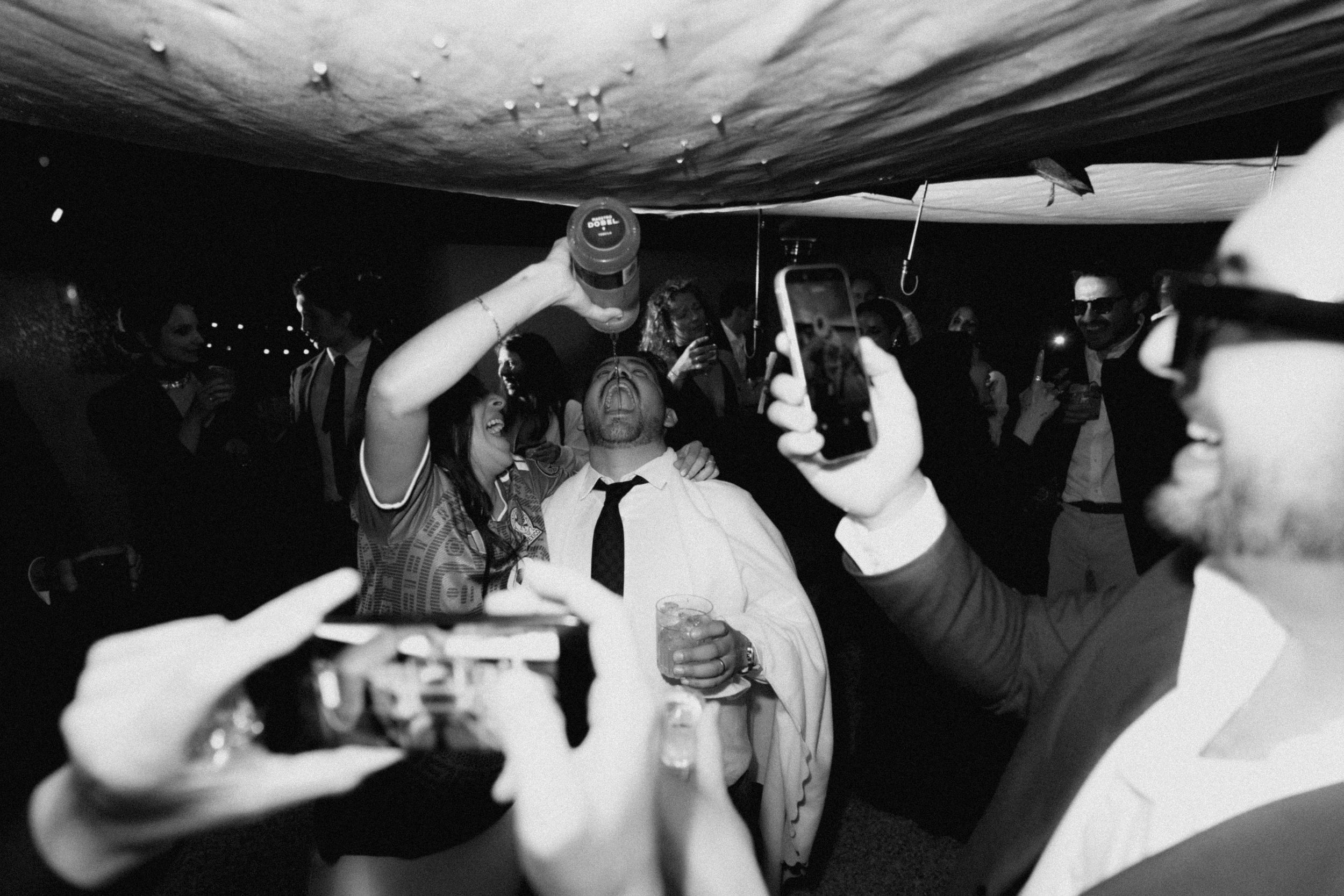 Black and white photo of wedding guests dancing and celebrating at a lively reception party.