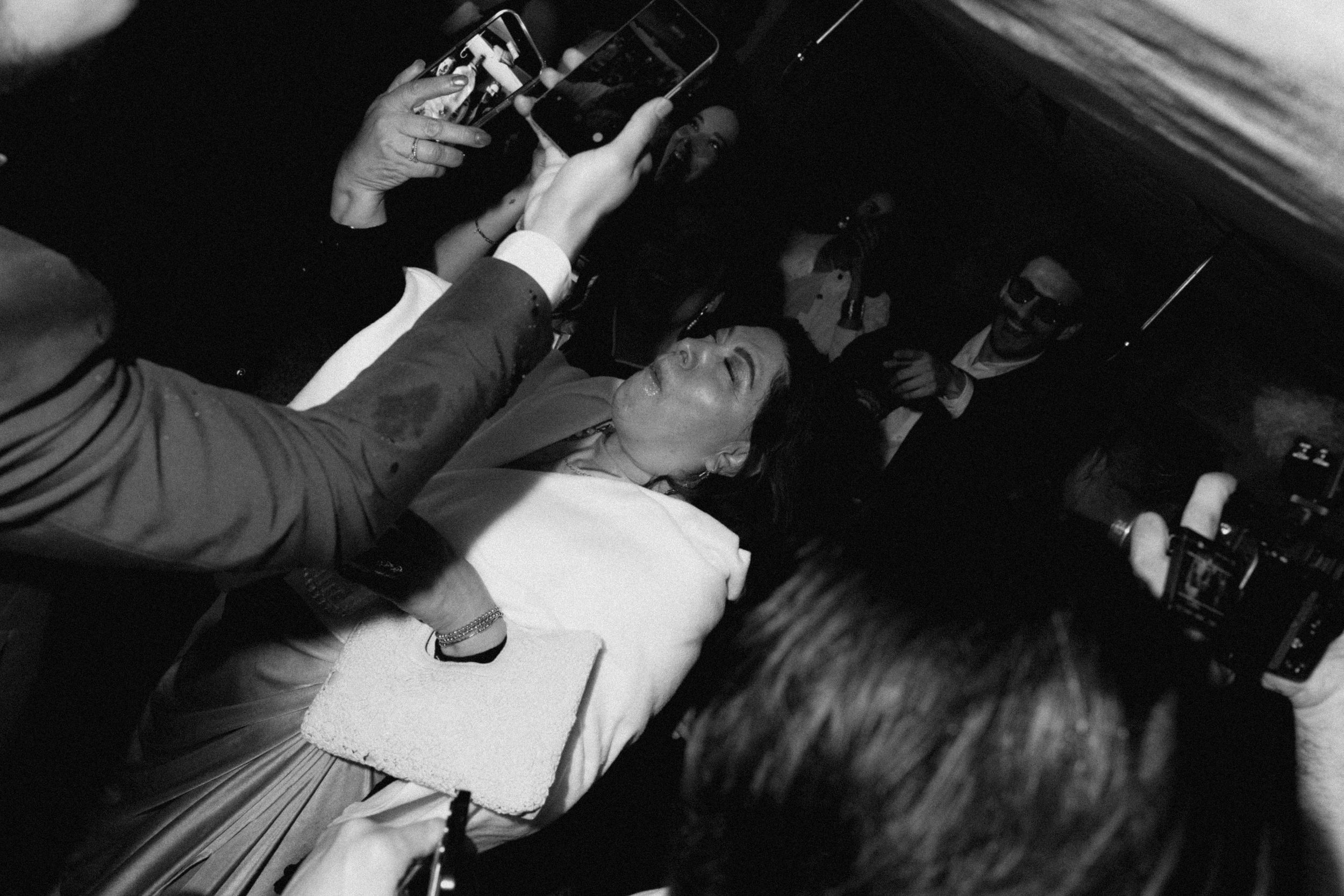 Black and white photo of a crowded event with people in formal attire, cameras raised, capturing a lively social gathering.