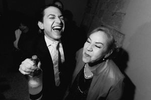 Black and white photo of laughing man holding bottle and woman at lively party celebration.
